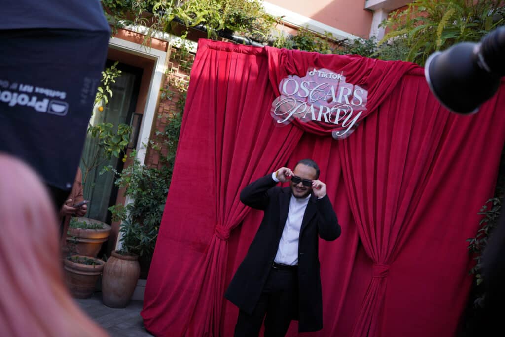 Gentleman in fornt about to take a picture in front of the TikTok Oscars Viewing Party Backdrop