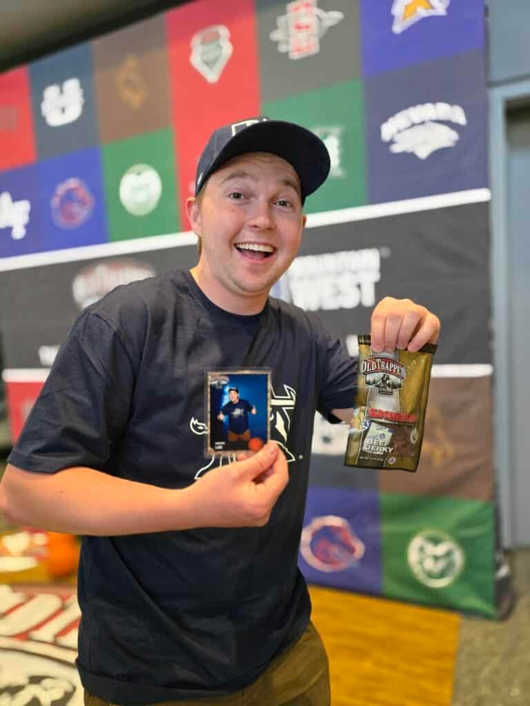 Excited young guy holding his trading card and Old trapper beef jerky at the Mountain West Basketball Tournament 2025