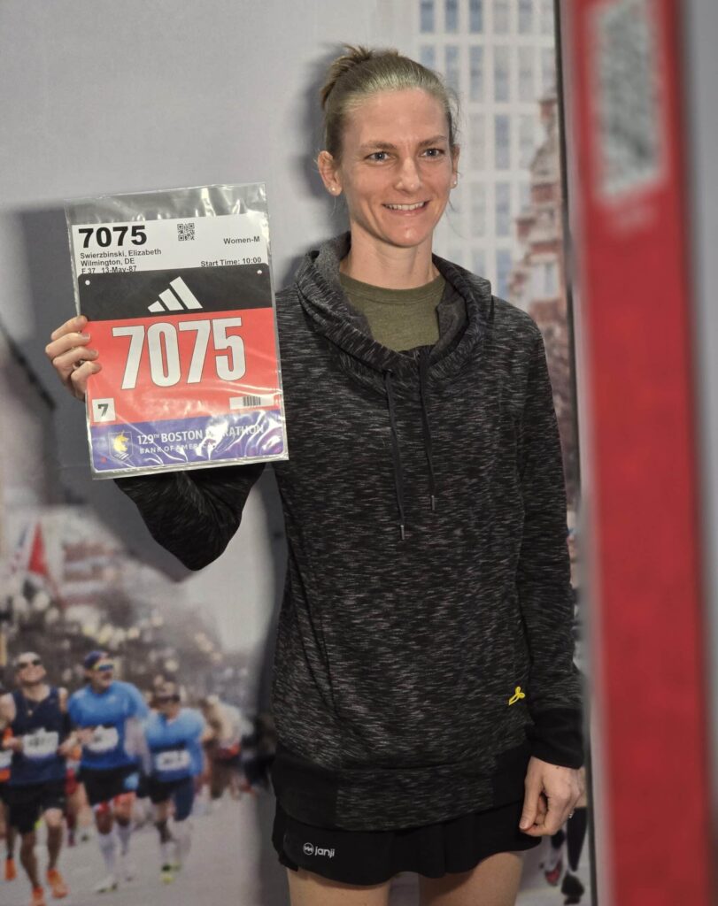 A lady competinmg in the Boston Marathon 2025 holding her number in front of the Photo Booth