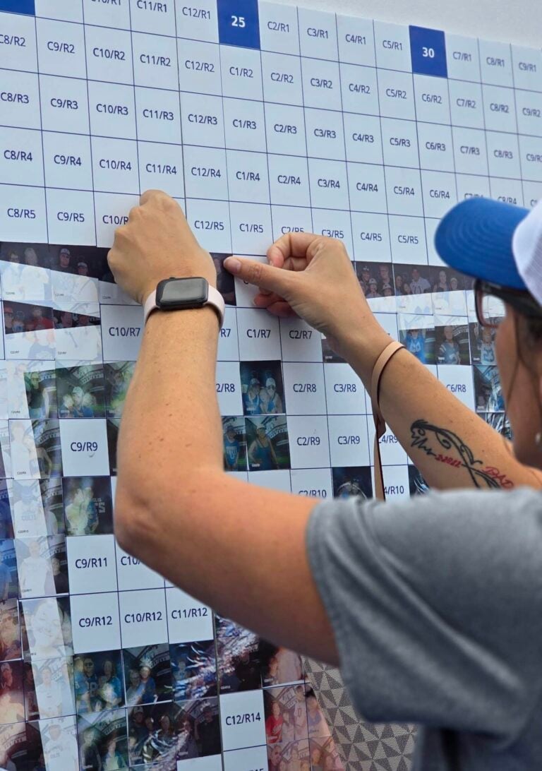 A person placing their photo tileon the big Photo Mosaic Wall for the Colts Training Camp 2025