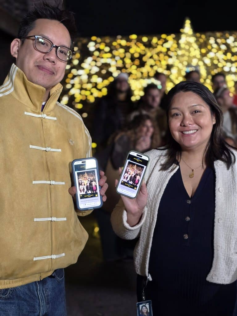 Couple happily holding their phones eith their digital photos at the Fox Holiday Party 2025