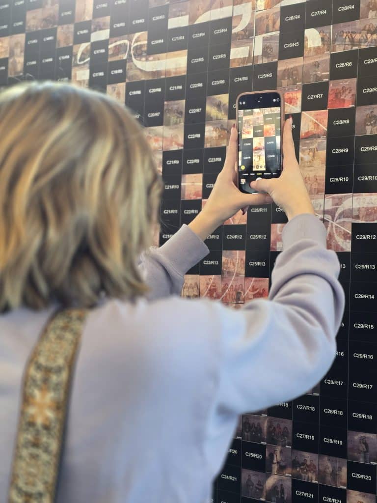 Seek 2026 Pic 6 A young girl taking a pictureof her print on the photo mosaic wall