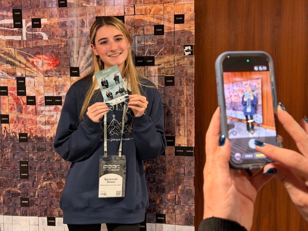A girl holding her Seek 2026 FOCUS print while someone is taking a picture of her with their phone