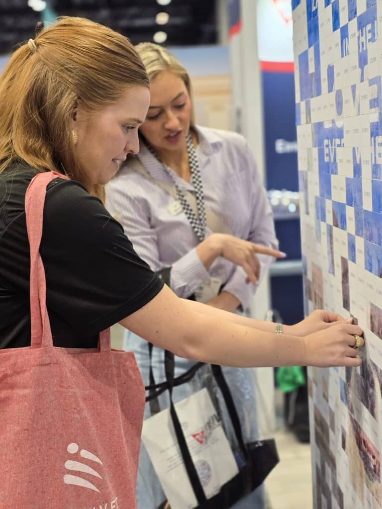 VMX 2026 Photo 5 A woman placing her sticker on the photo mosaic wall at VMX 2026