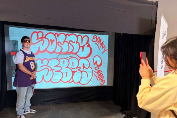 A lady taking a picture of a guy who just finished his artwork at he Graffiti Wall